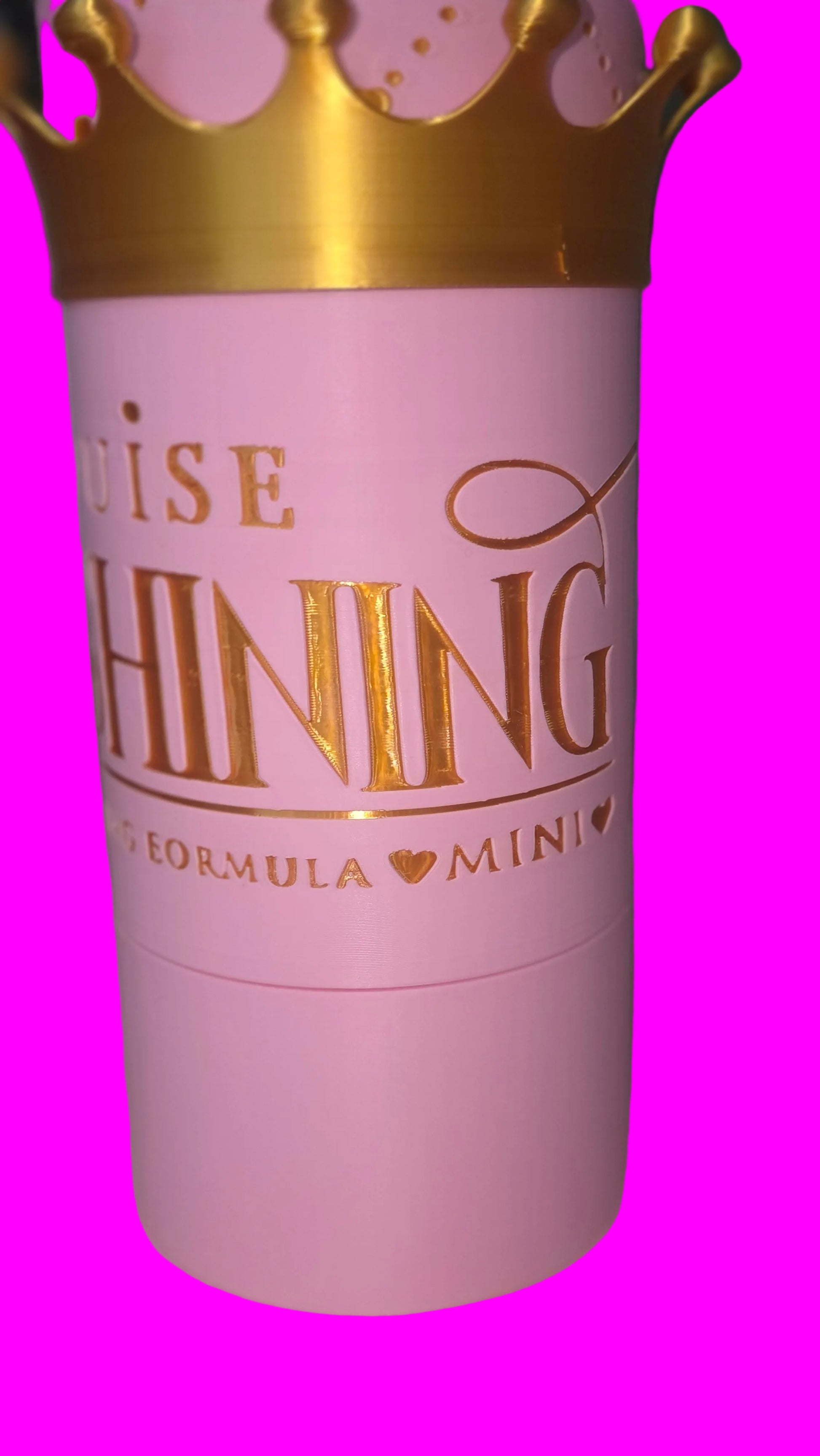 A close-up of a pink cylindrical cosmetic container with a gold crown at the top and gold lettering that reads 'RUISE SHINING' and 'FORMULA MINI'.