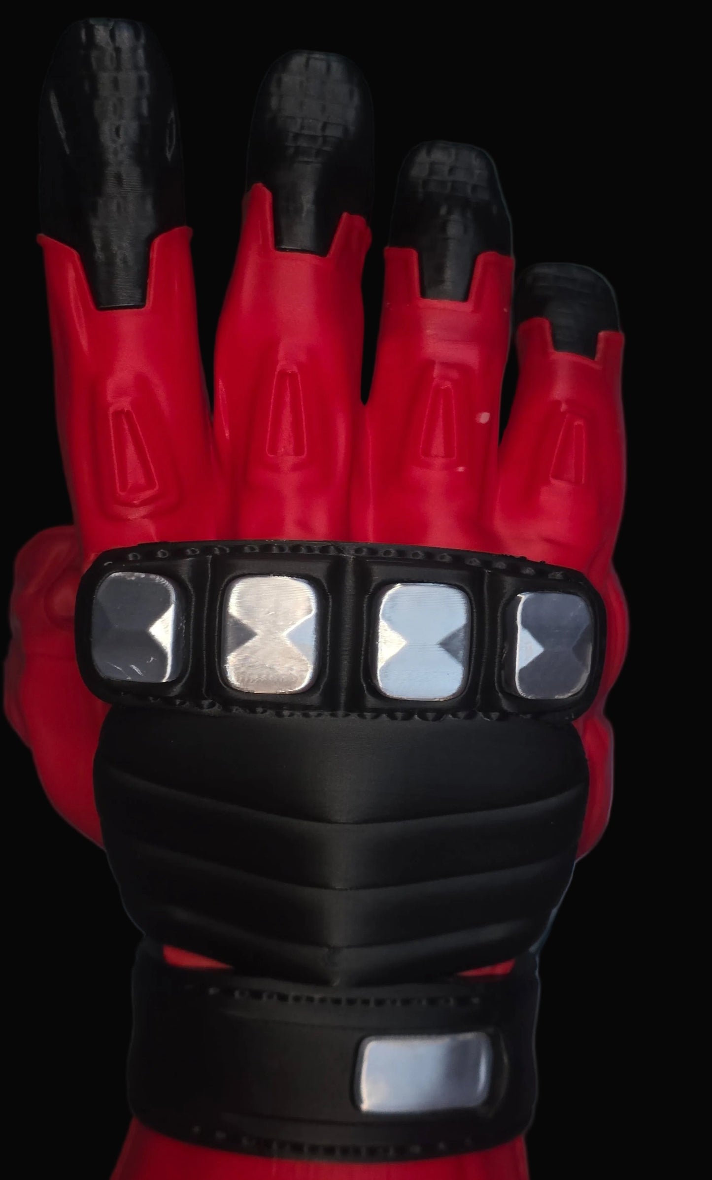 A close-up of a red and black futuristic glove with metallic silver accents on the wrist, shown against a dark gray background.